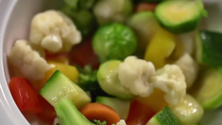 A variety of different vegetables including red peppers and broccoli are poured into a glass bowl