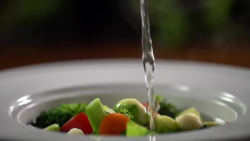 A ladle dumps water in a bowl of vegetables
