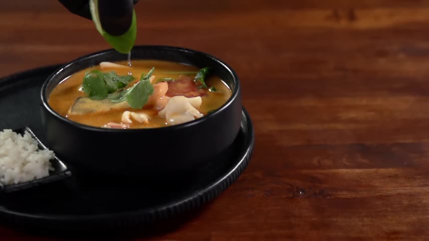 Liquid being poured on a bowl of soup sitting on a table at a restaurant