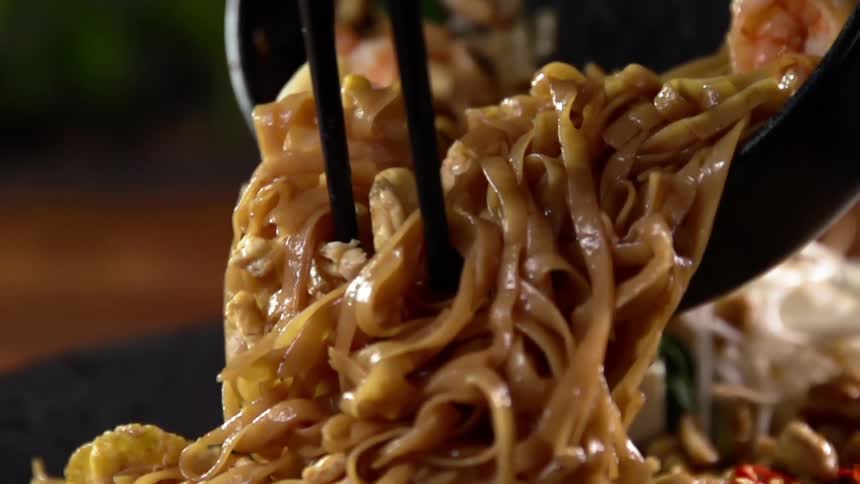 Noodles being served from a cast iron pan into a plate over a wooden table