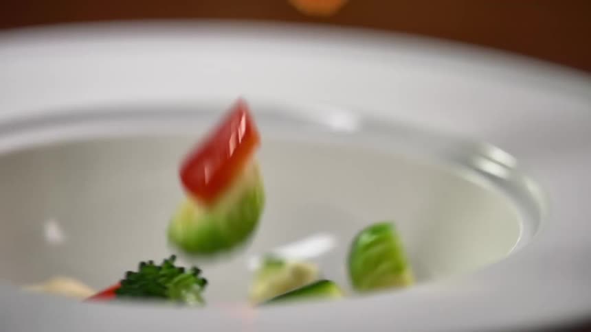 Various vegetable chunks fall into a white bowl