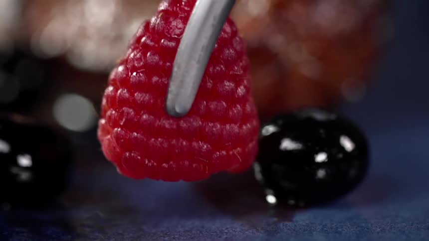 A raspberry is gently placed around a pastry using tongs