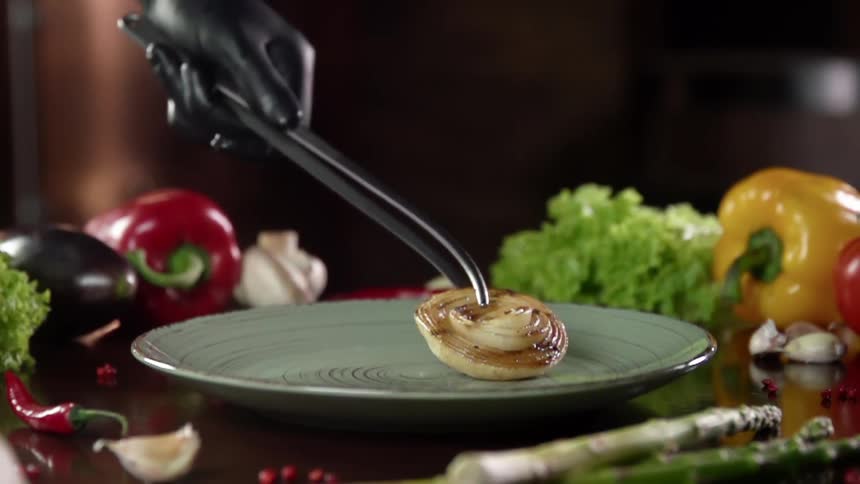 A grilled onion is placed on a teal plate surrounded by vegetables