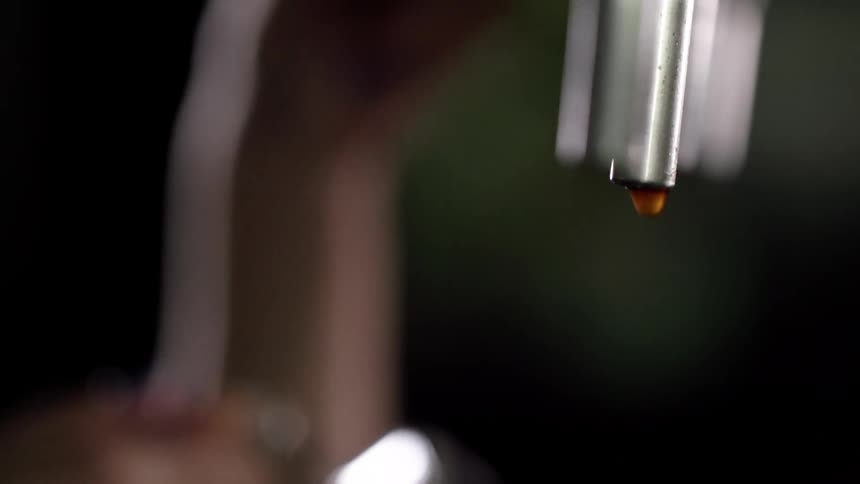 A person places a beer glass under the tap while drips of beer fall down