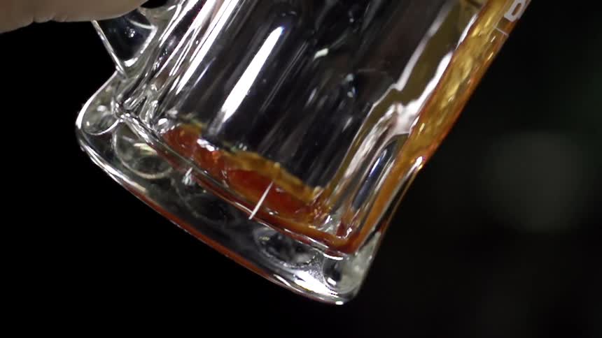 A brown drink is being poured into a jug standing out against the dark background