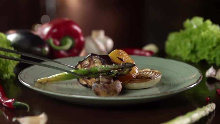A pair of tongs places asparagus on a dinner plate with seafood and vegetables