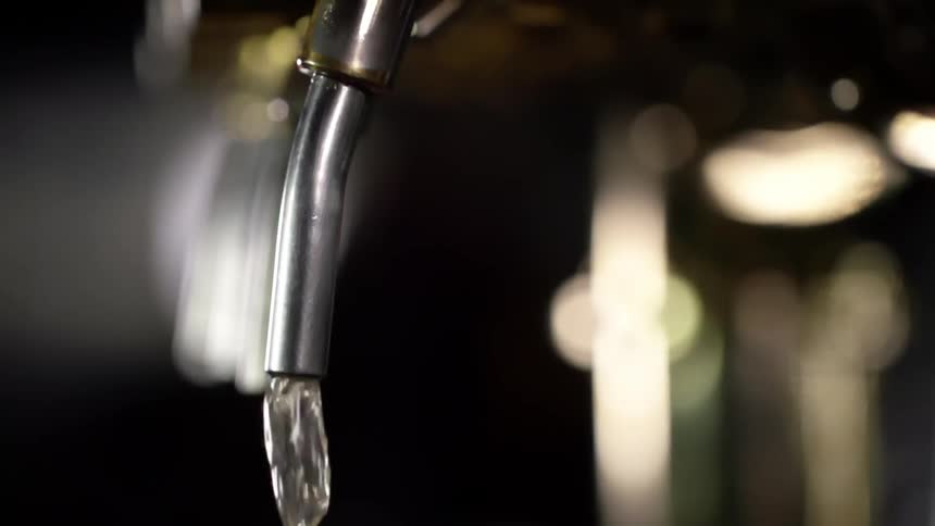 Beer bubbles and pours out of a metal tap
