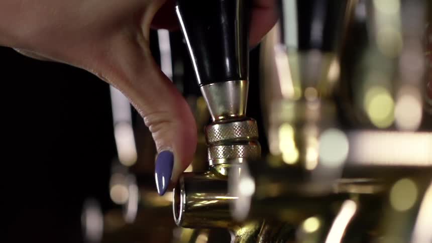 A woman in a bar pulls the lever on a beer tap