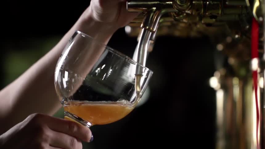 A bartender fills a tilted glass with beer from a tap