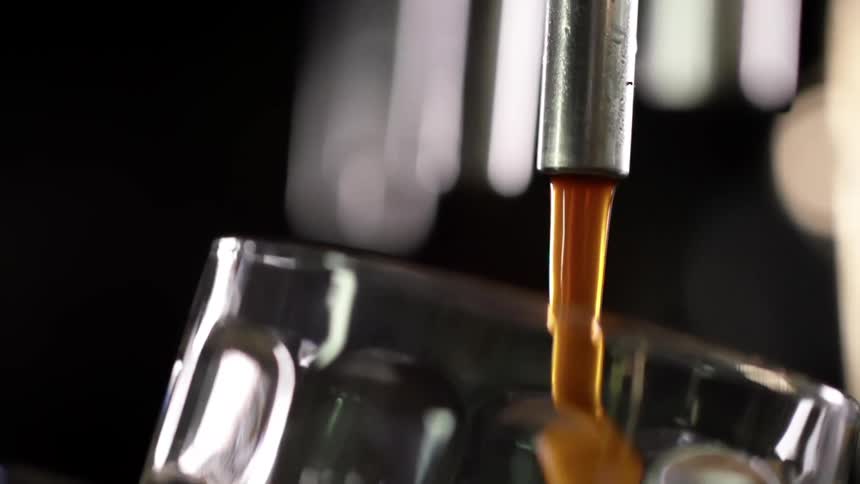 A think amber liquid pours from a tap into a clear glass