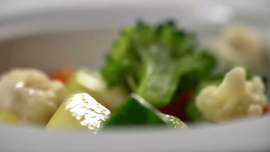 Vegetables fall into a white bowl to create a salad