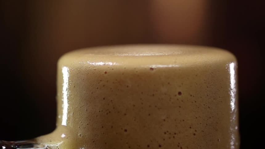 Brown liquid foam overflows in a glass mug