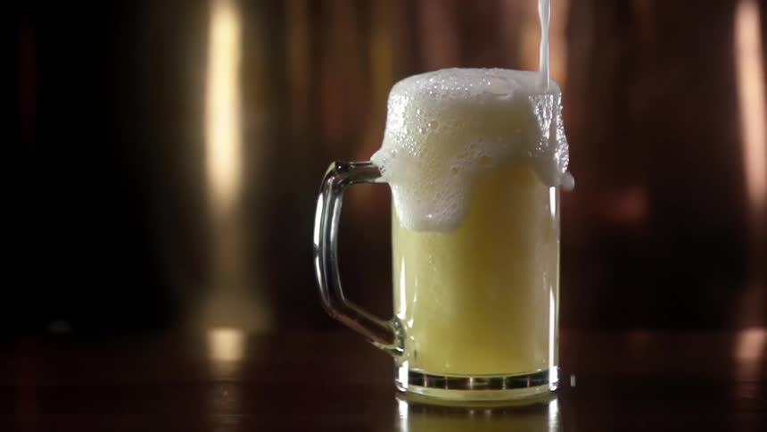 Beer overflows a glass mug sitting on a table