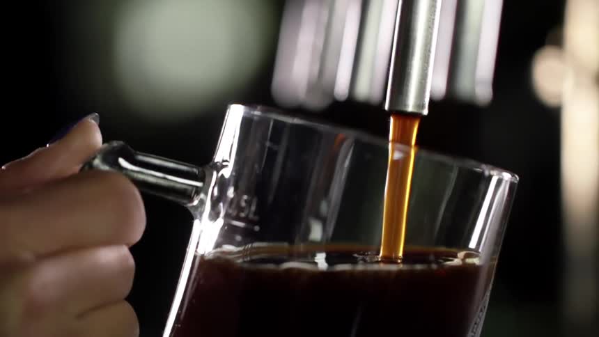 A white woman fills a glass mug with a brown liquid