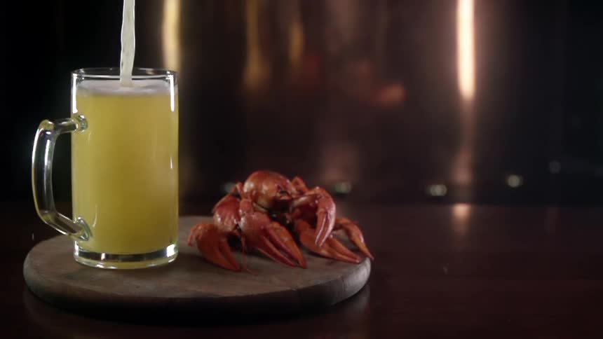 A piece of seafood and a mug filling with beer sit on a wooden board on a table