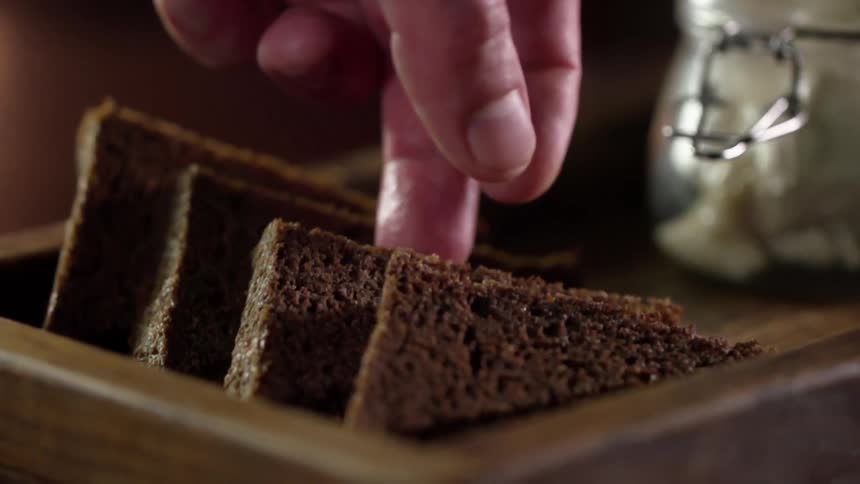 A white male stacks coarse brown bread on a wooden tray