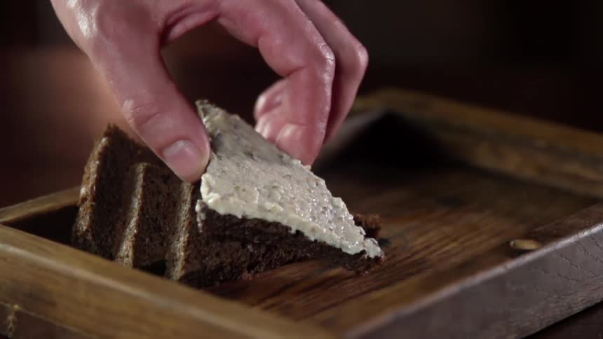 A white male sets a piece of bread covered in spread into a wooden tray