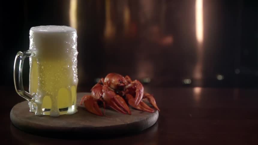 Beer foaming out of a beer glass next to crab legs over a wooden board in a counter