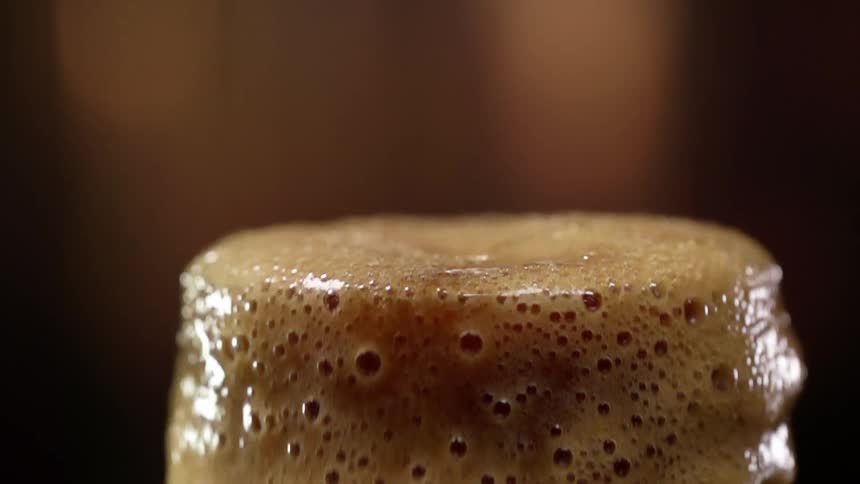 Dark beer pouring in a glass overflows and spills out