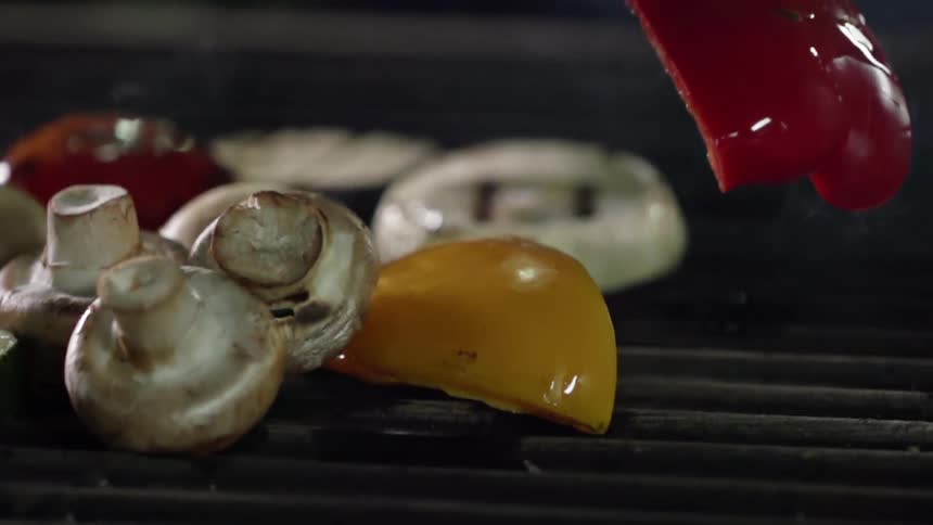 Assorted vegetables being grilled over smoking coals are turned upside down with tongs