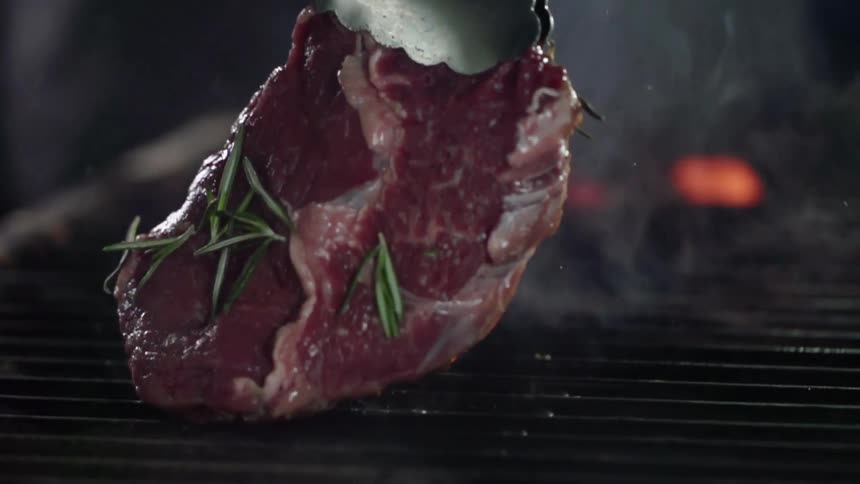 Raw seasoned red meat grilling over fire turned upside down with tong