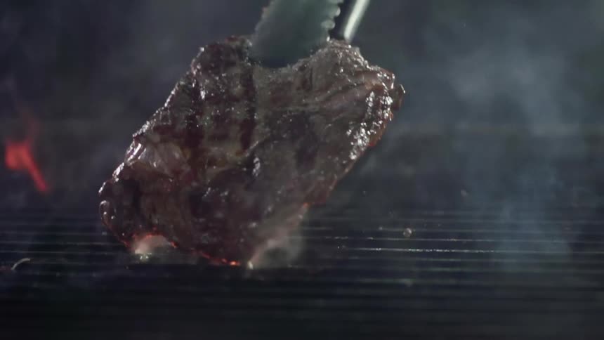A juicy steak is lift from the surface of a grill using a pair of metal tong