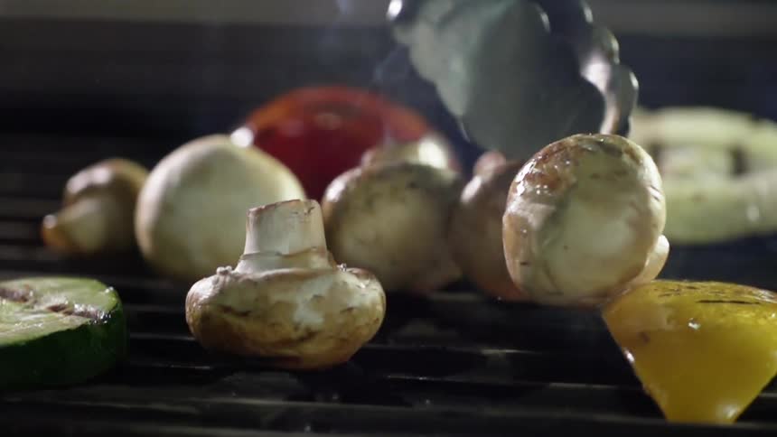 Tongs flipping mushrooms on a grill in slow motion