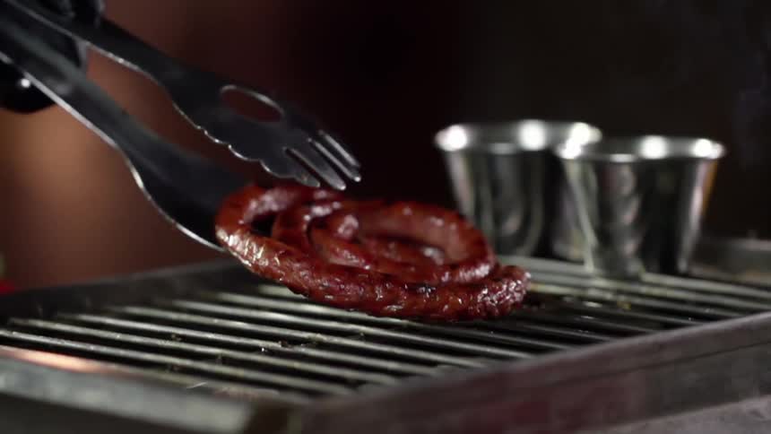 A person puts sausage on a grill