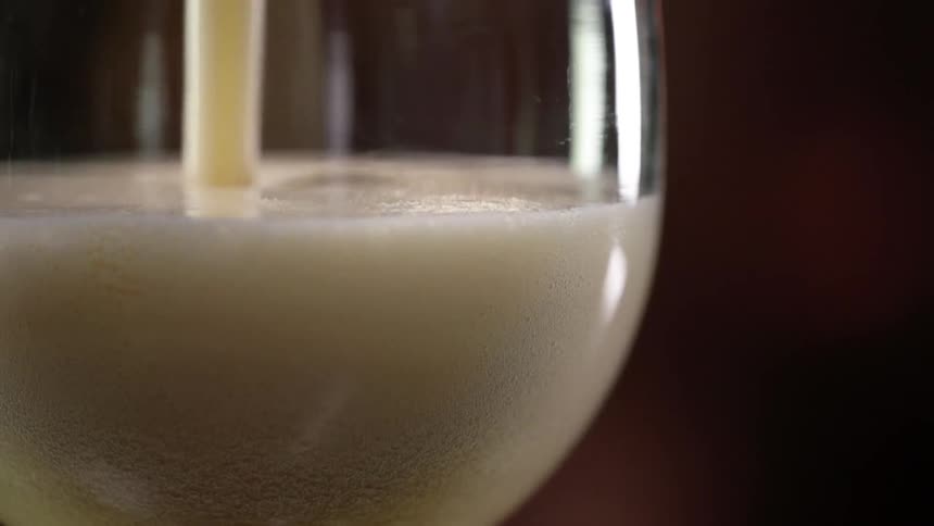 A glass is slowly filled up by a foaming bubbly liquid that is poured from above