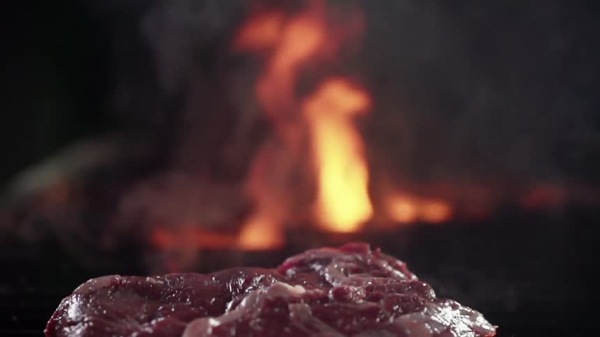A piece of meat is dropped on a grill with open flames
