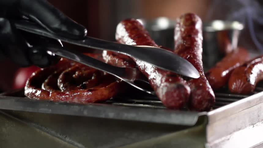 A person places sausages on a grill
