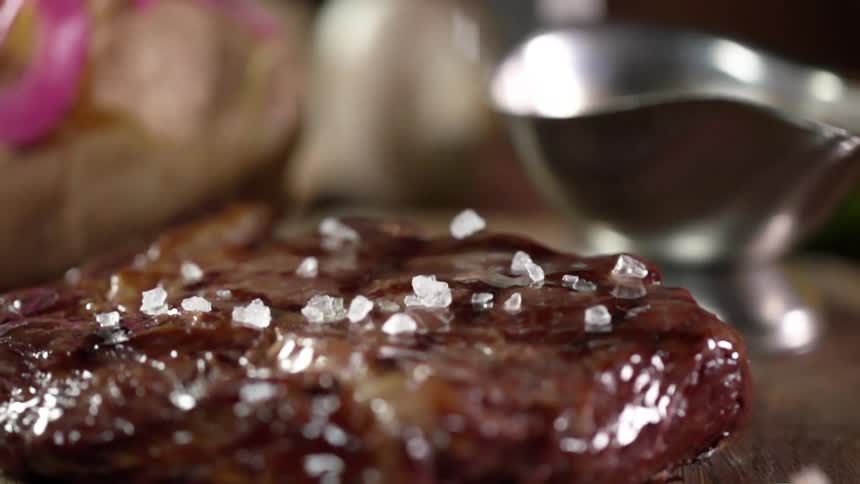Sea salt crystals bounce off the glistening brown cooked steak