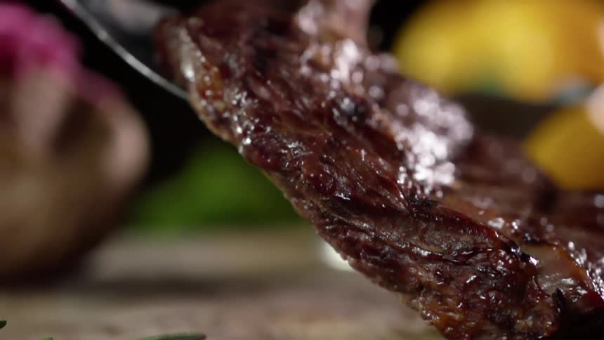 A person drops a cooked steak on a table using tongs