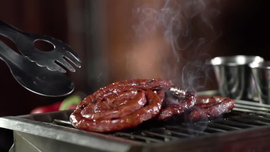 A pile of sausage cooks on a small grill