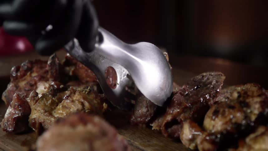 Chef wearing black latex gloves places pieces of cooked meat over the table with tongs