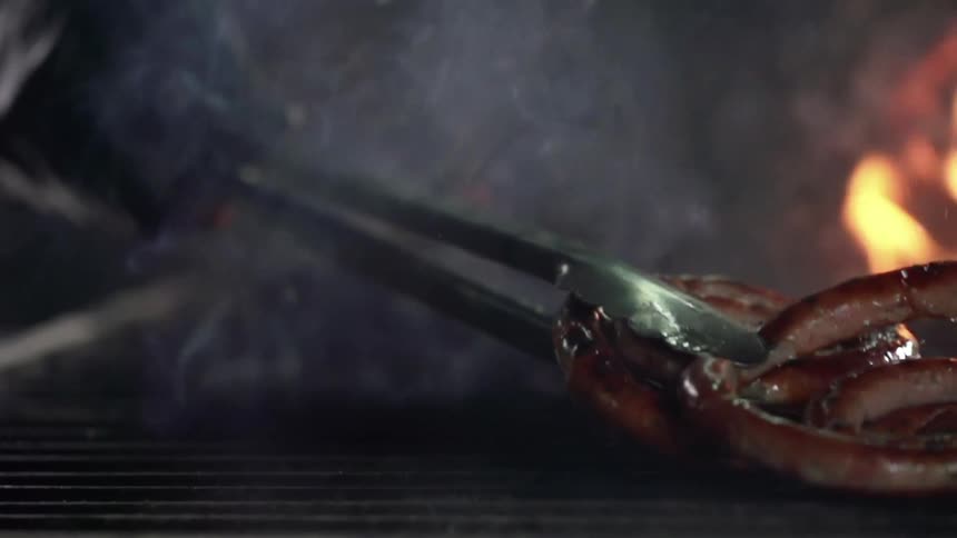 A person wearing a black glove pulls sausage off of a grill with tongs