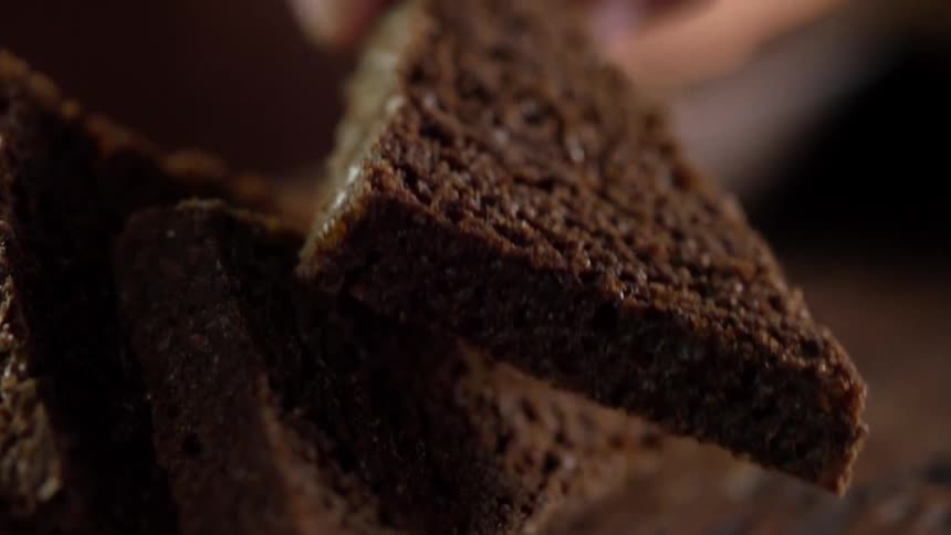Hand picks up a triangular slice of brown cake from the table