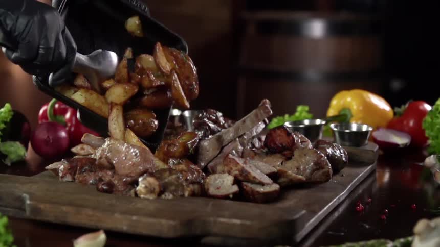 Gloved hands spoon steak fries onto a serving board with chopped steak