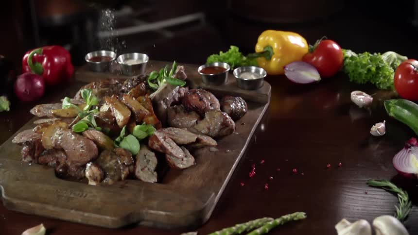 Salt is sprinkled onto chopped meat and mushrooms on a serving board with dipping sauces