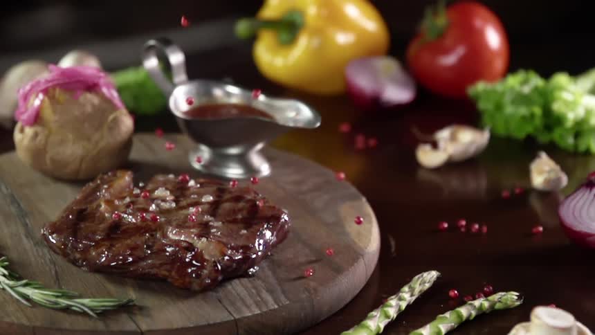 Seasoning is sprinkled onto a cooked piece of meat next to vegetables