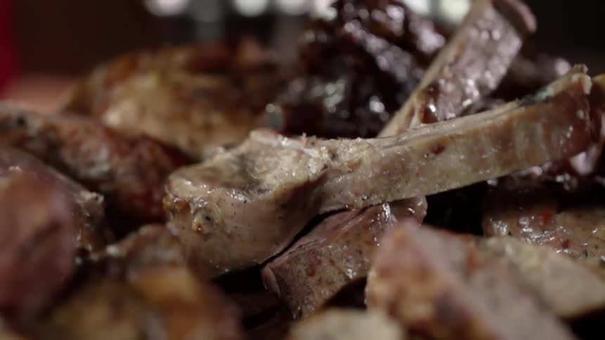 Pieces of cooked red meat piled on a plate using tongs
