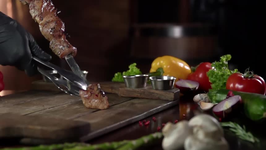 Pieces of cooked meat on a skewer are pulled off with tongs