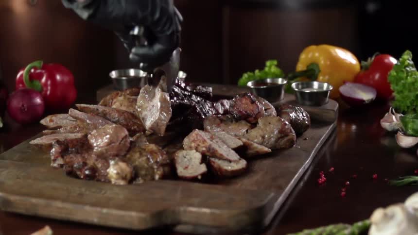 A person wearing a black glove drops a strip of dark meat onto a platter with a pair of tongs