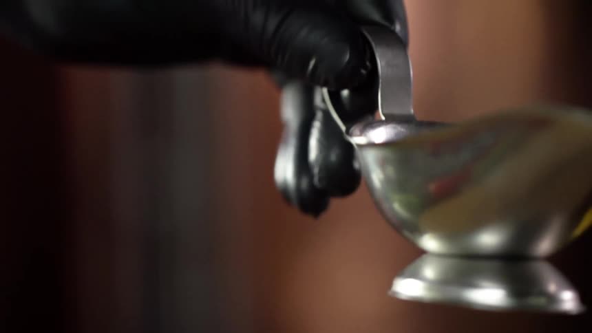 A person wearing black disposable gloves gently lowers a metal gravy boat