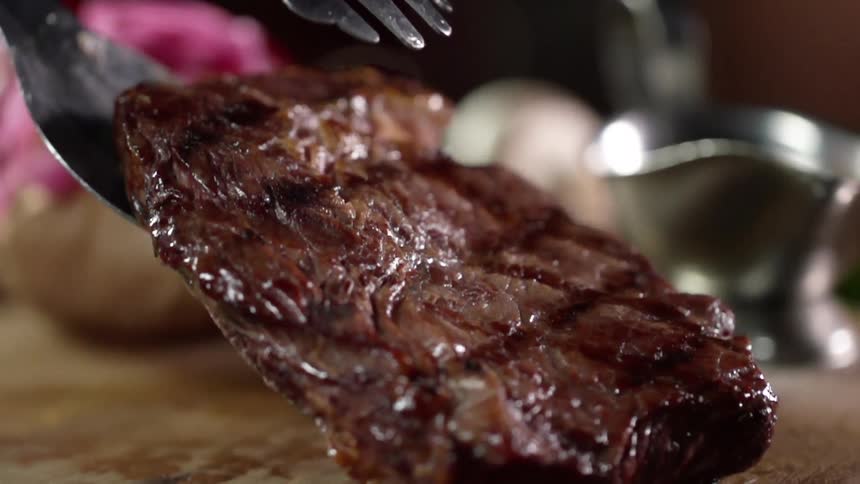 Grilled steak placed over a wood board with tongs