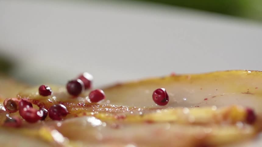Red berries fall on a slice of meat on a plate