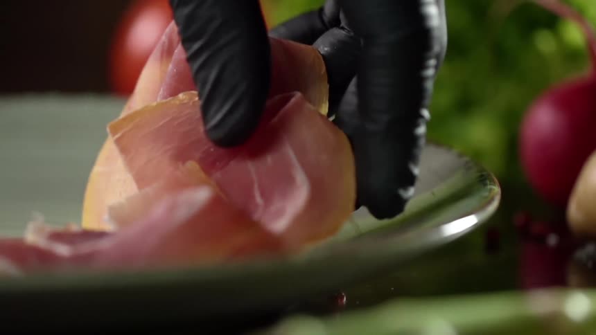A person wearing a black gloves puts thinly sliced meat on a plate