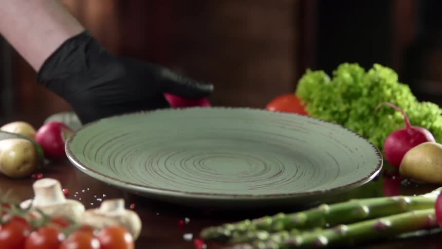 Black gloved hand places a plate near the vegetables