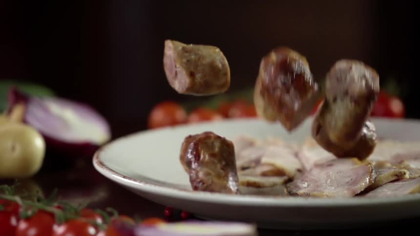 Sliced bits of sausage fall onto a plate surrounded by cherry tomatoes