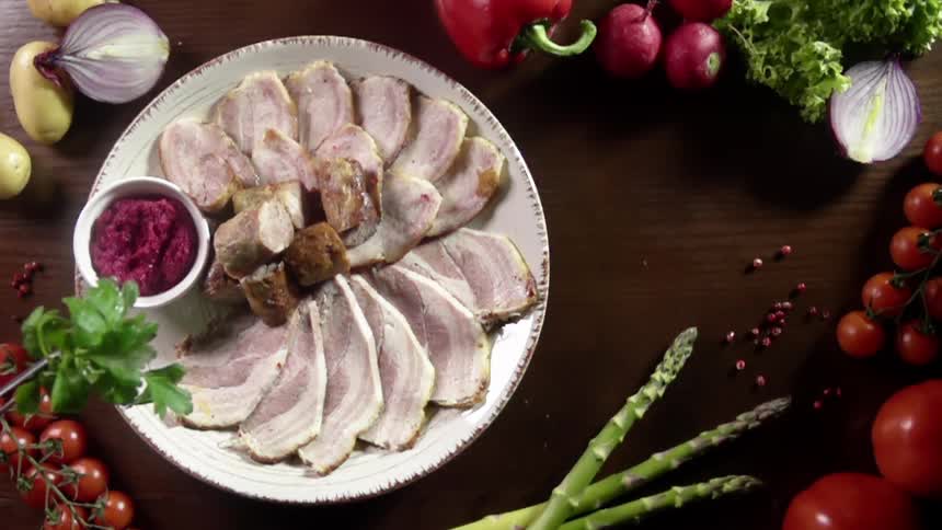 A large meat platter sits amid a display of various vegetables